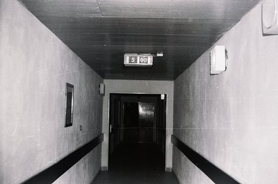 Mid-century institutional hallway with concrete walls and ceiling, featuring a digital floor clock displaying "5:00." Plain d...