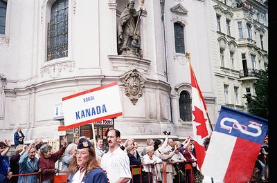 Neoclassical building facade with Baroque statues flanking entrance, crowded with people holding signs and flags. Prominent "...