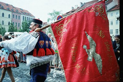 Traditional folk festival participant in ornate attire, carrying a red banner with gold embroidery and a stylized eagle motif...