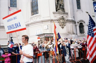 Crowd rally near grand neoclassical building with "Sightseeing Tour" signage. Participants hold flags: American, Polish, and ...