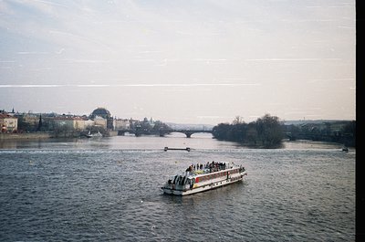 Vintage riverboat with passengers cruising Prague’s Vltava River, framed by historic bridges and Baroque architecture. Overca...