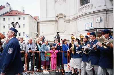 Vienna street scene featuring a brass band in coordinated navy uniforms with white accents, playing near a historic Baroque-s...
