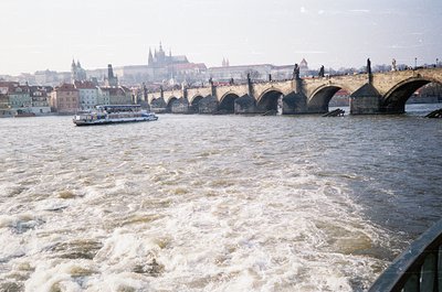 Historic Charles Bridge spanning Prague’s Vltava River, featuring Gothic towers and statues. Classic 1960s/70s color film gra...