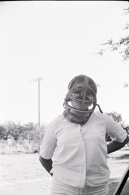 Baseball catcher in vintage mask and checkered shirt, standing outdoors. Classic 1960s-1970s sportswear and protective gear. ...