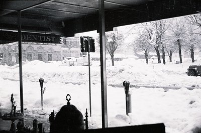 Snow-covered urban street corner with vintage signage: "DENTIST" (International Bank of Austria) and "REAL ESTATE" visible. B...