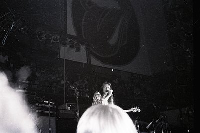 Black-and-white concert shot featuring a vocalist in a flowing white dress, microphone in hand, under dramatic stage lighting...