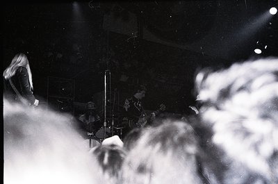 Blurred black-and-white shot of a live jazz band in dimly lit venue, featuring saxophonist and drummer. Crowd silhouetted in ...