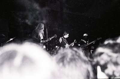 Black-and-white live band performance with dense stage smoke. Three musicians—guitarist (center), bassist (left), and drummer...