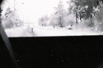 Blurred monochrome shot of a snowy winter scene viewed through a windowpane, showing indistinct figures walking on a snow-cov...
