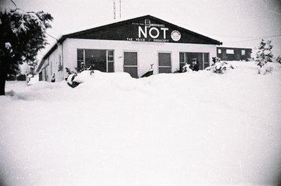 Mid-century brick building blanketed in snow, featuring bold signage: "NOT THE VOICE OF FRESNO." Single-story with large wind...