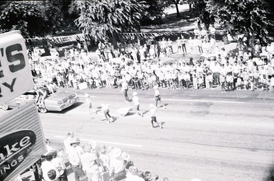Vintage black-and-white street scene featuring a chaotic, crowded race with participants in shorts and caps. Spectators line ...