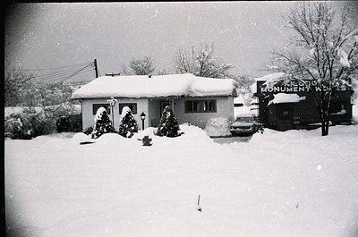 Mid-century suburban home blanketed in snow, featuring a single-story ranch-style design with arched windows. Decorated with ...