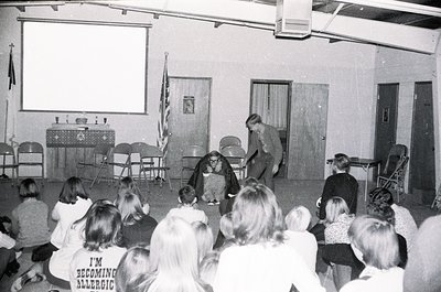 Black-and-white classroom scene featuring a teacher demonstrating science experiment with liquid nitrogen to a seated audienc...