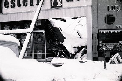 Snow-damaged storefront with collapsed roof and signage reading "Western Auto" and "Pot Liquor." Visible vintage products lik...