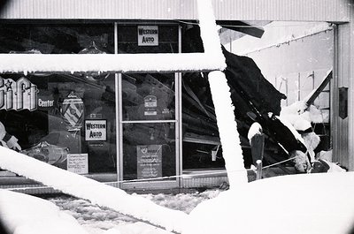 Snow-damaged storefront with "Western Auto" signage and shattered glass, likely mid-20th century. Visible branding includes "...