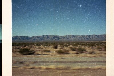 Vintage desert landscape with distant mountain range under clear sky, captured through aged film grain. Dry terrain with spar...