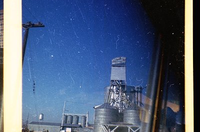 Vintage industrial scene featuring a grain elevator with "A. G. Sperry & Sons Co." signage, likely mid-20th century. Silhouet...