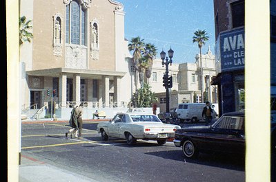 Vintage street scene featuring Art Deco-style building with arched windows and decorative stonework. Palm trees line the side...