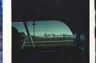 Vintage car interior shot through windshield, showing blurred rural landscape with dense greenery and a faint road. Tinted gl...