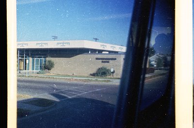 Mid-century modern building with curved concrete roof and large windows, viewed through a vehicle window. Likely a public or ...