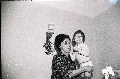 Vintage black-and-white photo of an adult holding a laughing child indoors, likely mid-20th century. Floral wallpaper and a w...