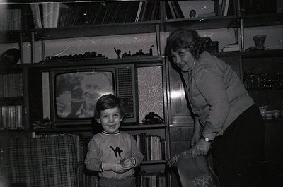 Mid-20th century living room scene: a woman in a patterned blouse and a boy in a sweater pose beside a vintage CRT TV (1960s-...