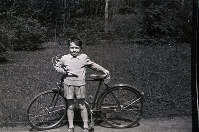 Vintage black-and-white photo of a young girl (approx. 6-8 years) posing beside a classic 10-speed bicycle in an outdoor sett...