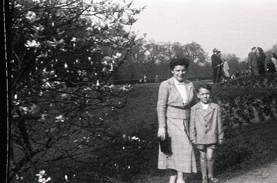 Mid-20th century black-and-white photo of a woman and young boy in a park setting. Woman wears a knee-length dress with a bel...