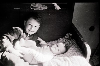Black-and-white snapshot of two boys in a vintage crib, one holding a younger sibling. Mid-20th century domestic setting, lik...