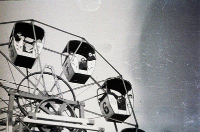 Vintage amusement park swing ride with enclosed gondolas, numbered "6" visible. Two people seated, mid-ride, against a blurre...