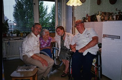 Four adults pose indoors in a mid-century home, likely Eastern Europe, 1970s–1980s. A man and woman in wheelchairs sit beside...