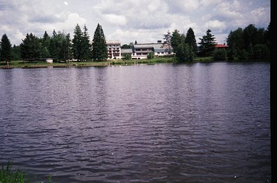 Lakefront view of a mid-20th century resort complex with modernist architecture. Low-rise buildings with flat roofs and large...