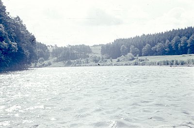 Frozen lake bordered by snow-laden forest and open fields under overcast skies. *(Note: The sepia tone suggests potential vin...