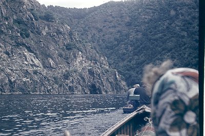 Vintage black-and-white shot of a rocky coastal landscape with steep cliffs and a small boat on calm waters. Partial view of ...