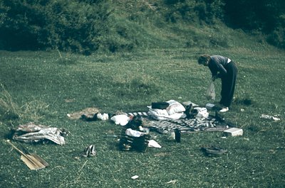 Mid-century outdoor picnic scene with vintage clothing and camping gear. A person in a striped sweater and dark pants organiz...