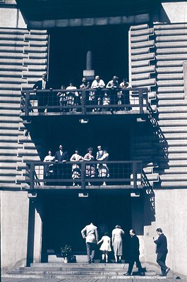 Black-and-white photo of a multi-level outdoor staircase gathering, likely 1950s–1960s. Two groups: one seated on upper balco...