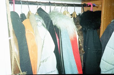 Vintage winter clothing rack featuring fur-lined coats, wool jackets, and synthetic parkas. Hanging hooks show signs of wear,...