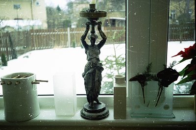 Vintage ceramic lamp with classical female figure holding candle holder, placed on a frosted window sill. Snow-covered garden...