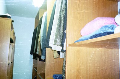 Minimalist wooden closet with vintage storage—hanging coats, folded jeans, and a pink sweater on shelves. Functional, utilita...