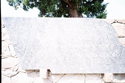 Marble slab with speckled veining, likely Carrara or similar, set against rough-hewn stone blocks. Natural outdoor lighting h...