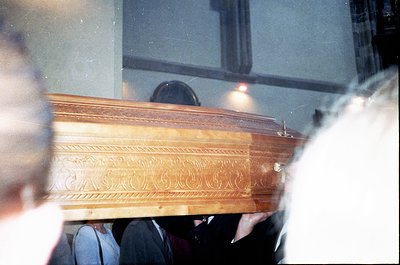 Vintage close-up of an ornate wooden casket with classical scrollwork, viewed through a slightly blurred window. Indoor setti...