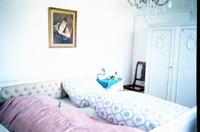 Vintage bedroom featuring a double bed with floral-patterned bedding and a single decorative pillow. Above the bed hangs a fr...