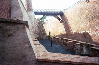 Industrial courtyard with exposed brick and concrete staircases leading to a raised platform. A metal bridge spans the upper ...
