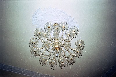 Art deco chandelier with intricate floral metalwork and crystal accents, mounted on a textured ceiling. Likely from mid-20th ...