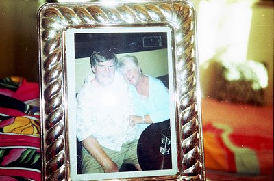 Vintage framed photo of two individuals in casual 1970s attire—man in a light shirt and khakis, woman in a floral blouse—posi...