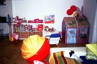 Vintage children’s playroom with mid-century play structures: cardboard house with floral details, toy shelves stocked with b...