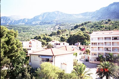Mid-20th century Mediterranean coastal village nestled between mountains and sea. Whitewashed buildings with terracotta roofs...