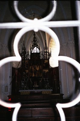 Baroque-style altar framed by ornate ironwork, featuring intricate carvings, candle holders, and religious iconography. Gothi...