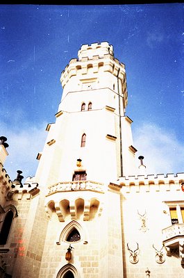 Gothic-style tower with crenellated parapets, arched windows, and decorative deer antlers flanking the entrance. Lighting sug...