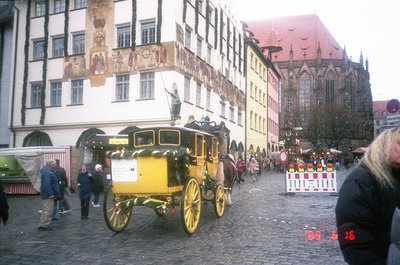 Historic yellow horse-drawn carriage navigating a cobblestone square in Nuremberg, Germany. Surrounding buildings feature med...